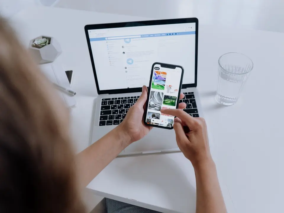 Osoba drži mobitel ispred otvorenog laptopa